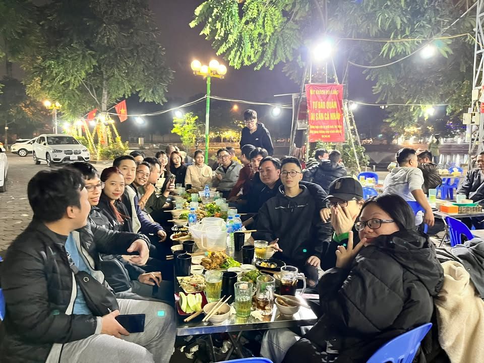 Đội VNTAY liên hoan ngoài trời buổi tối, bàn dài đông người và nhiều món ăn