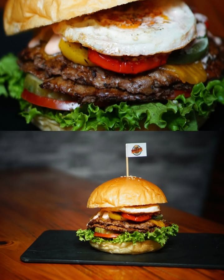 Burger bò hai tầng kẹp trứng ốp la, cà chua, đặt trên khay đá phiến cắm cờ thương hiệu