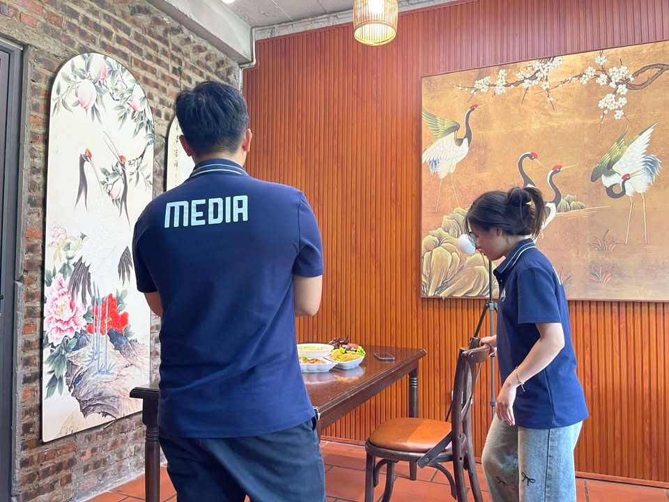 Nhân viên VNTAY mặc áo Media dàn dựng bàn chụp món trong phòng ăn treo tranh hạc
