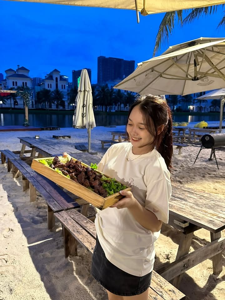 Cô gái bưng khay đồ nướng trên bãi cát ven hồ trong buổi chụp ngoài trời